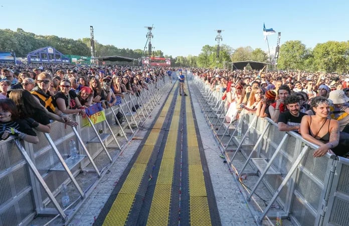 Publiek leunt tegen aluminium dranghekken langs een looppad voor het podium van een festival