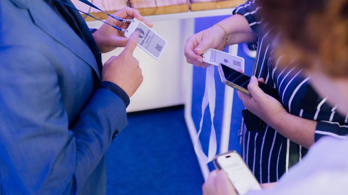 Twee bezoekers houden een digitale e-ink-badge met naam en QR-code vast en scannen die met een telefoon