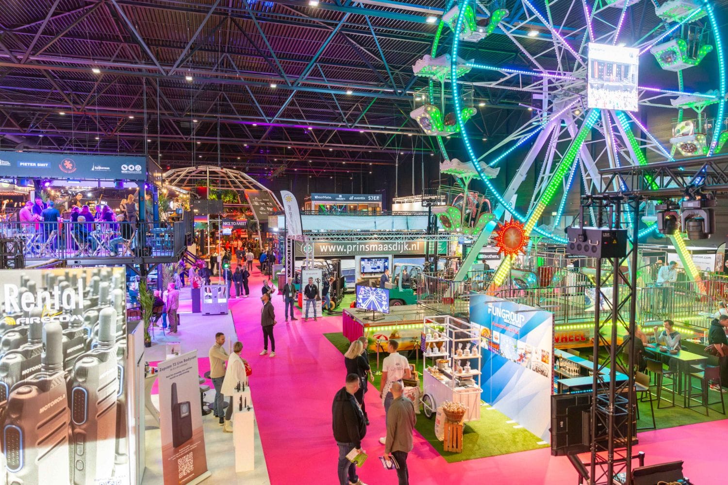 Beursvloer van Festivak in de Brabanthallen met stands, een verlicht reuzenrad en bezoekers op het roze tapijt