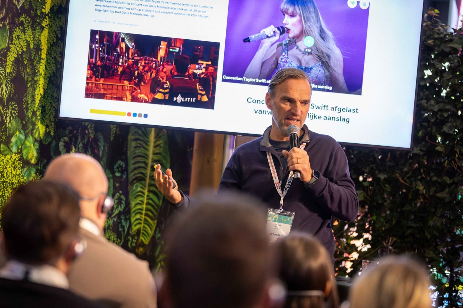 Spreker tijdens een kennissessie op Festivak, voor een groot scherm en een groene plantenwand