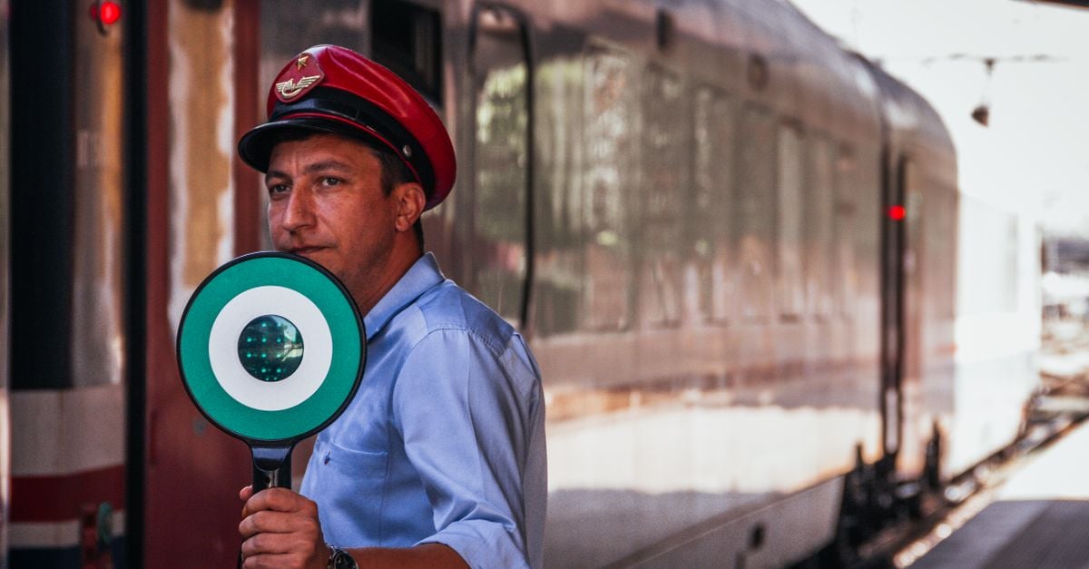 A train conductor at a station holding a signal for train departure.