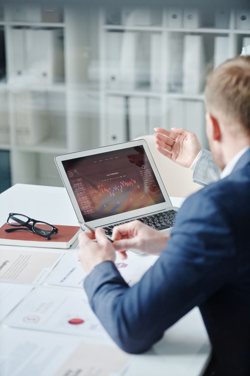 Twee professionals die een financiële analyse bespreken op een laptop in een modern kantoor.