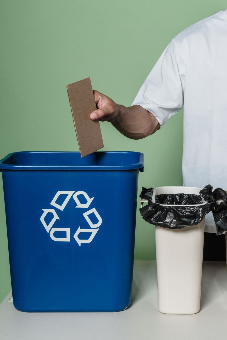 Een persoon plaatst karton in een blauwe recyclingbak, en bevordert milieuvriendelijke praktijken binnen.