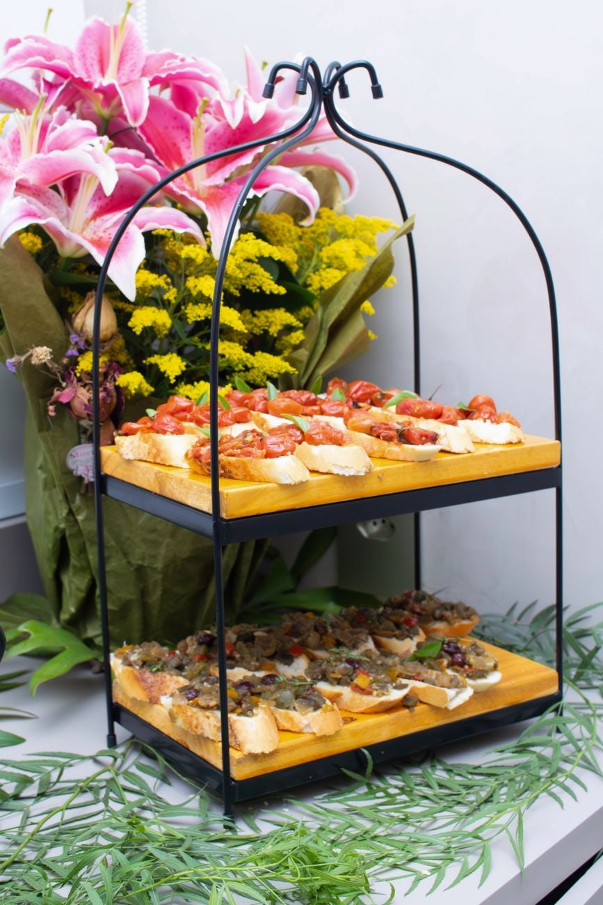 Artistieke schikking van hapjes op een tweelaagse standaard met levendige bloemen creëert een feestelijke sfeer.