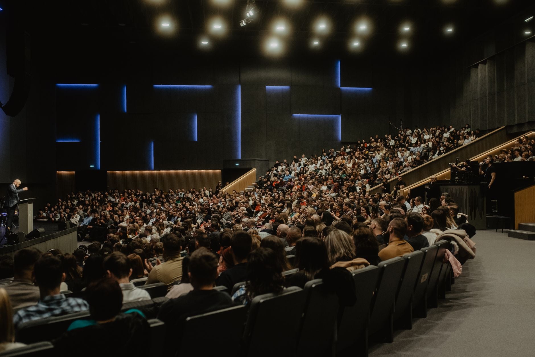 Een groot publiek luistert aandachtig naar een spreker op een conferentie in Oradea, Roemenië.