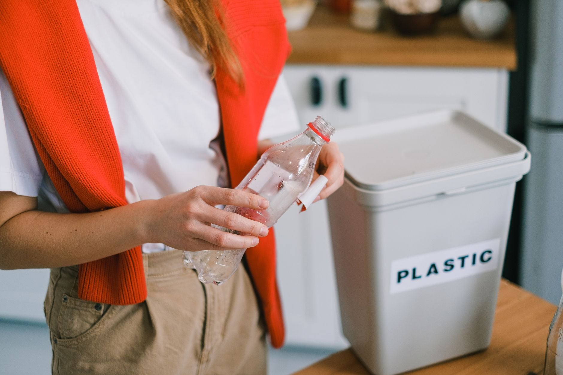 Vrouw plaatst plastic fles in recyclebak in keuken.