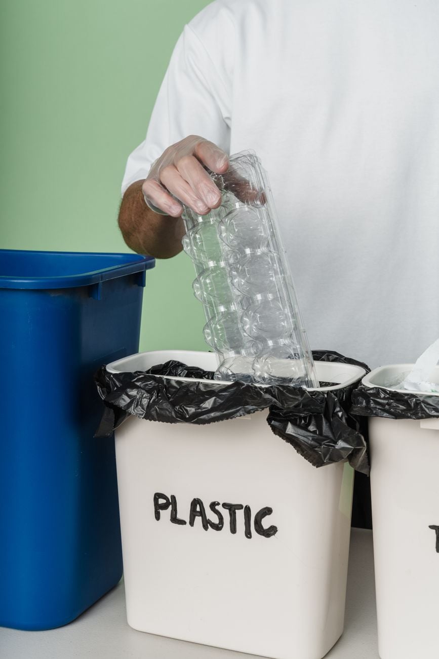Persoon die plastic container in de afvalbak recycleert, ter bevordering van duurzaamheid en afvalreductie.
