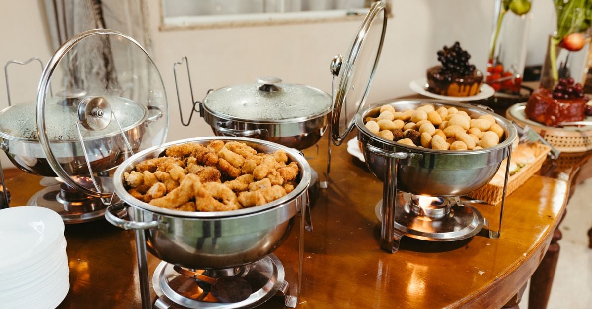 Een heerlijk buffet met diverse hapjes in warmhoudschalen op een houten tafel.