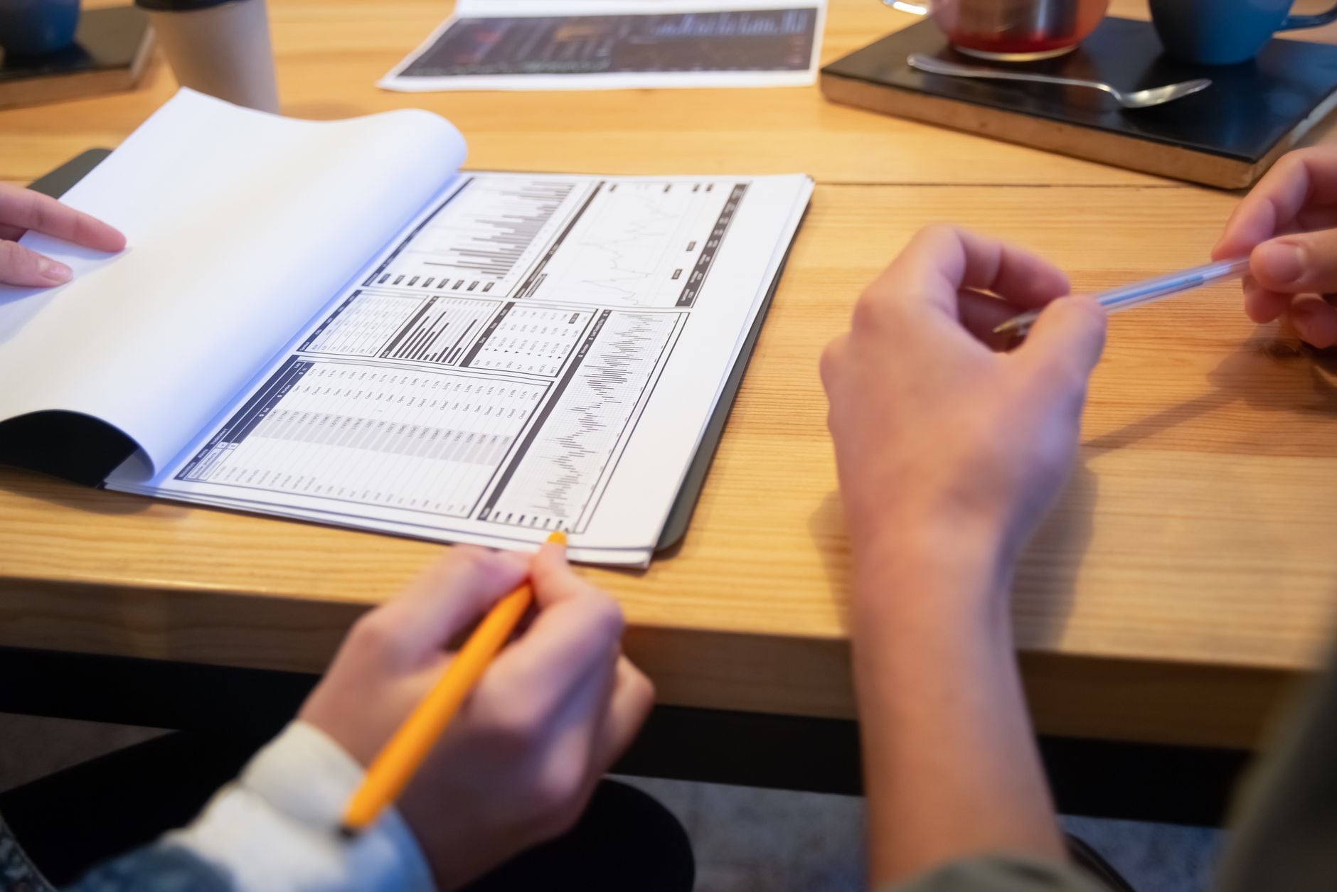 Close-up van collega's die analyses bekijken aan een houten tafel in een casual setting.