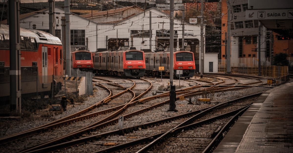 Stedelijk treinstation met rode treinen op meerdere sporen, waardoor een dynamisch en industrieel stadsbeeld ontstaat.