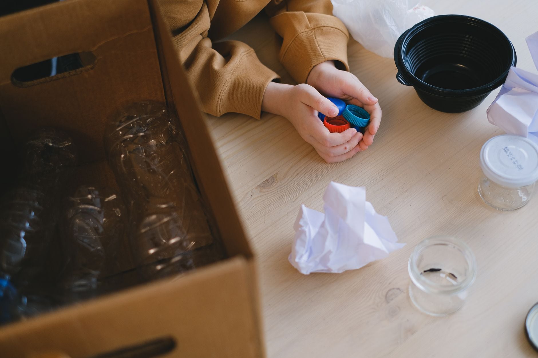 Persoon die recyclebare materialen zoals plastic deksels en papier op een tafel organiseert.
