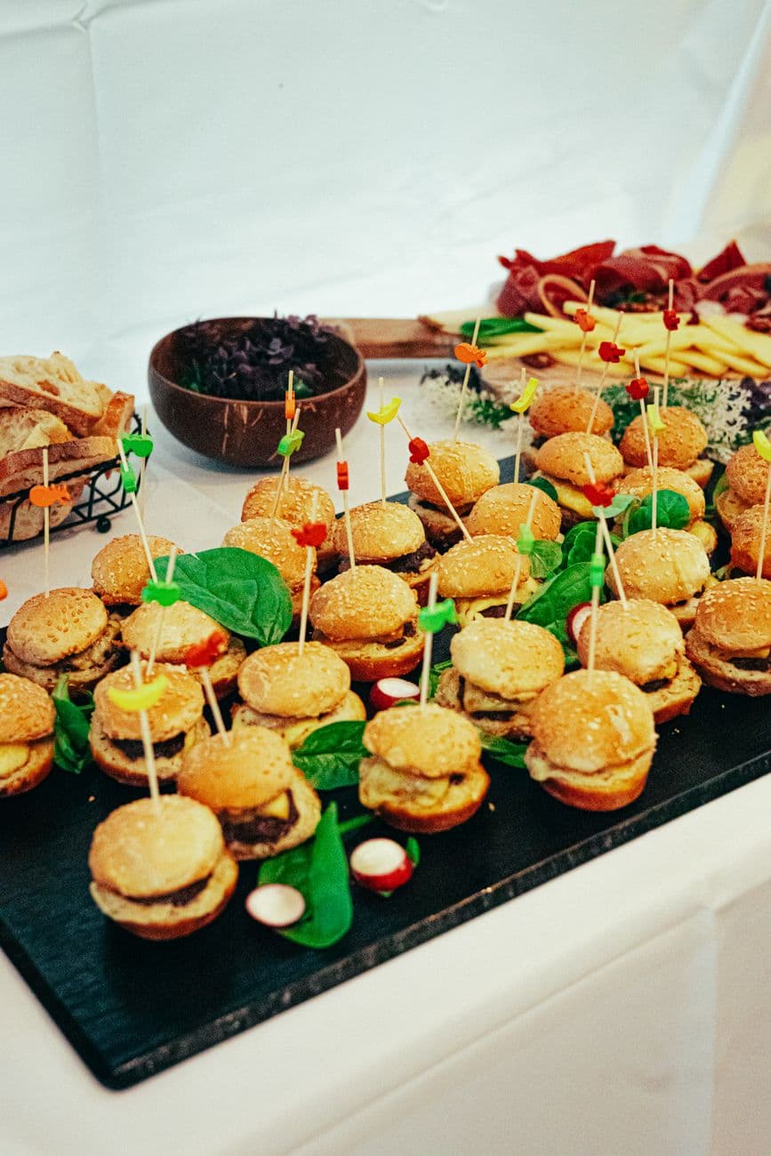 Een levendige presentatie van mini-hamburgers met spiesjes tijdens een cateringevenement, ter ondersteuning van de feestelijke presentatie van het eten.