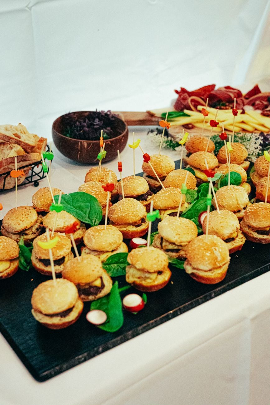 Een levendige presentatie van mini-hamburgers met spiesjes tijdens een cateringevenement, ter ondersteuning van de feestelijke presentatie van het eten.