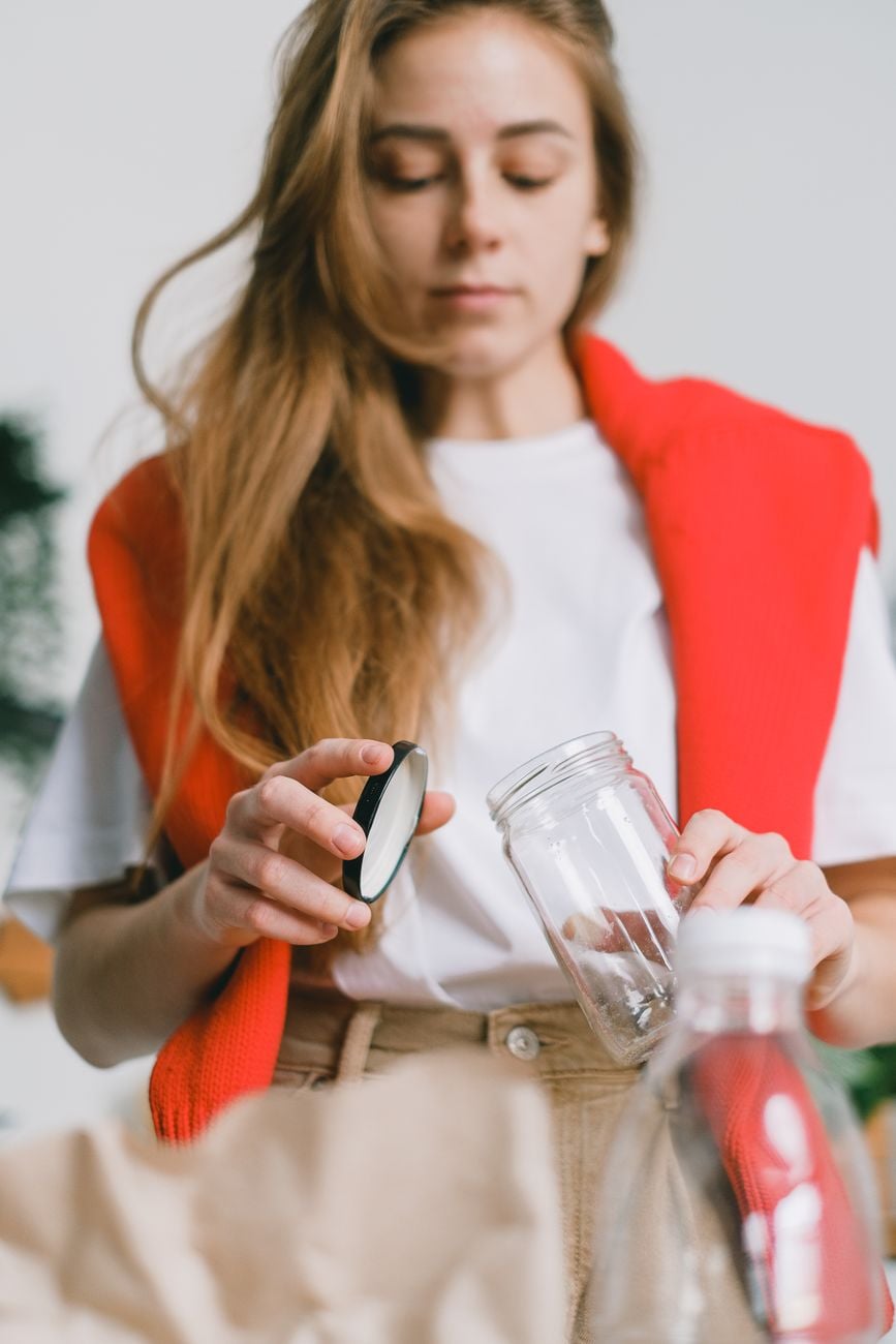 Een jonge vrouw sorteert verantwoordelijkheid recyclables in glazen potten voor een zero waste beheer.