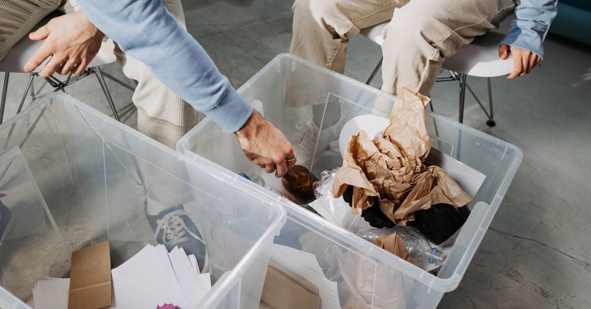 Close-up of hands sorting recyclable materials in clear plastic boxes indoors.