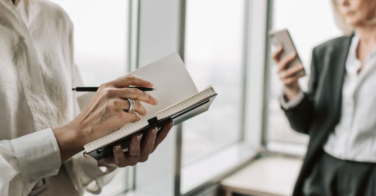 Businesswomen collaborating in an office setting, writing notes and using a smartphone.