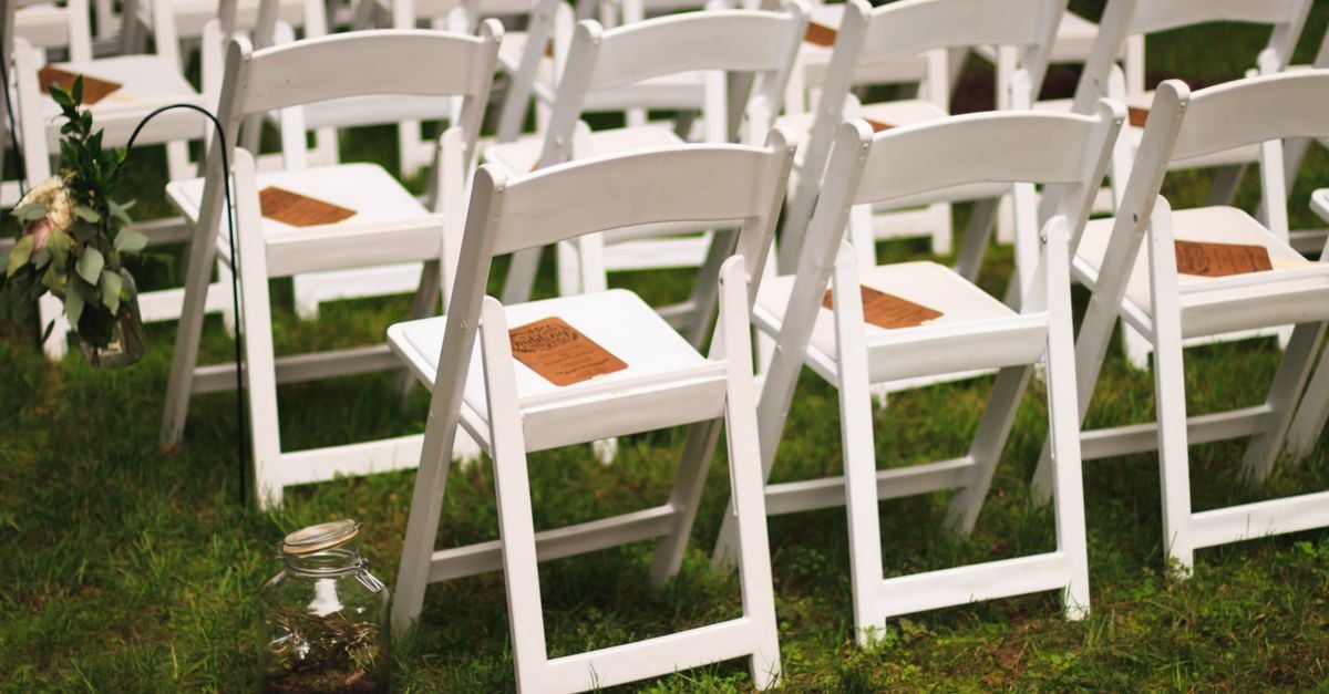 White wooden chairs arranged in a garden setting, perfect for an outdoor wedding or event.