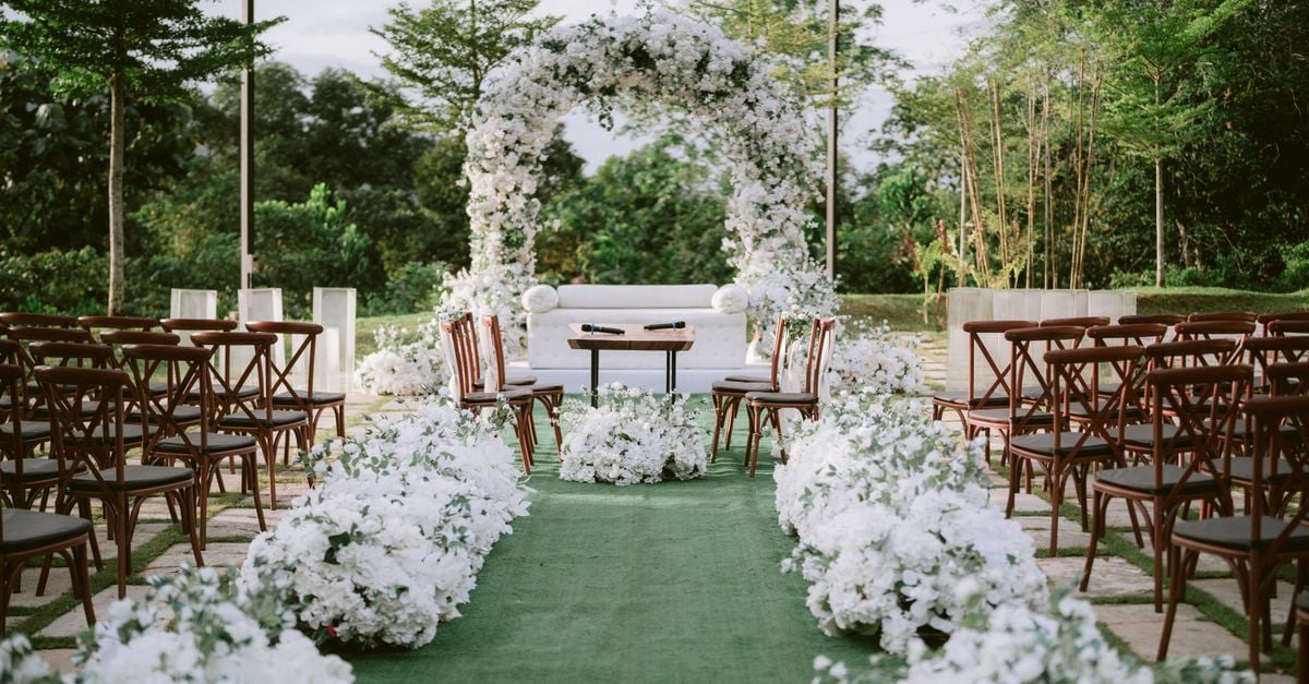 Beautiful outdoor wedding ceremony with white floral arch and chairs arranged beneath trees.