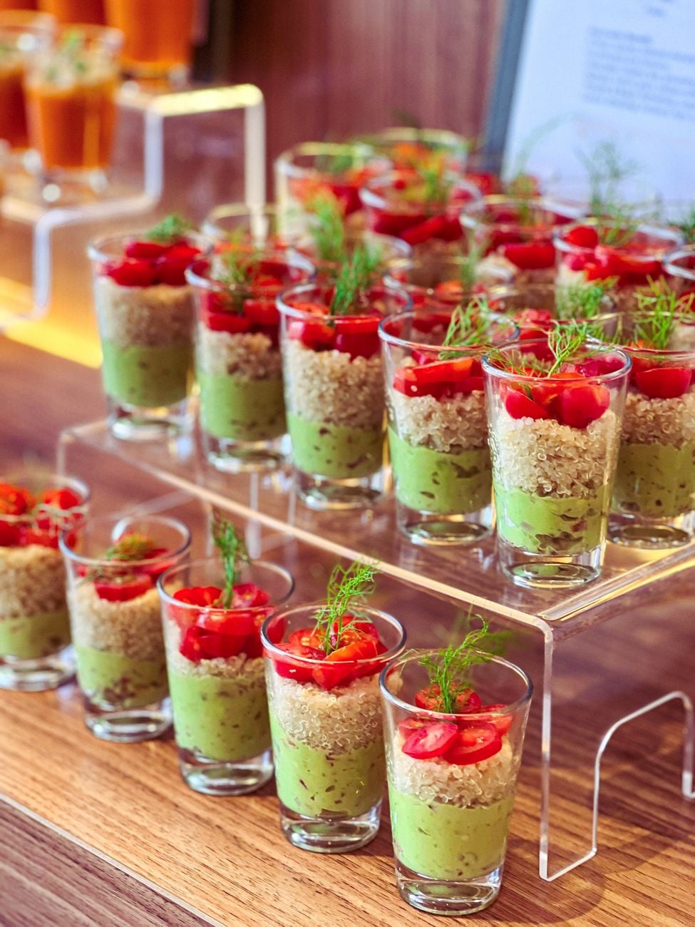 Levendige hapjes met avocado, quinoa en tomaat in shotglaasjes, perfect voor evenementen.