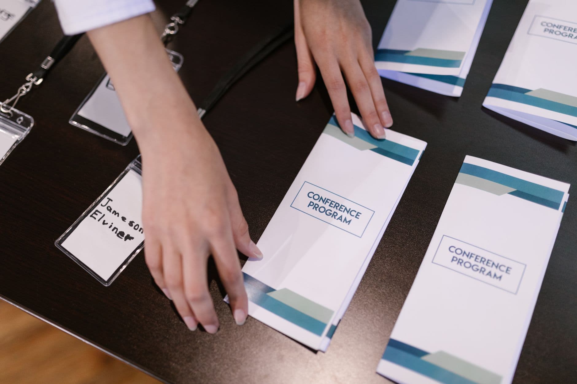 Handen die conferentieprogramma's en naamstickers organiseren aan de registratietafel.