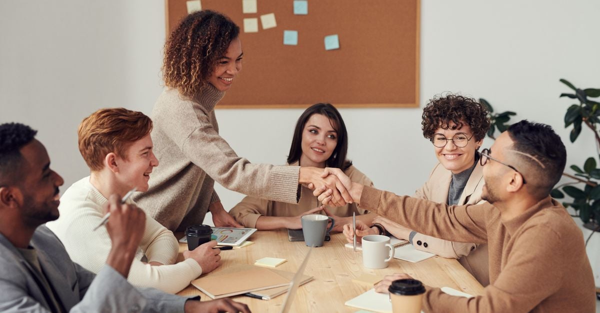 Eventprofessionals in overleg rond een vergadertafel, met een handdruk als teken van samenwerking