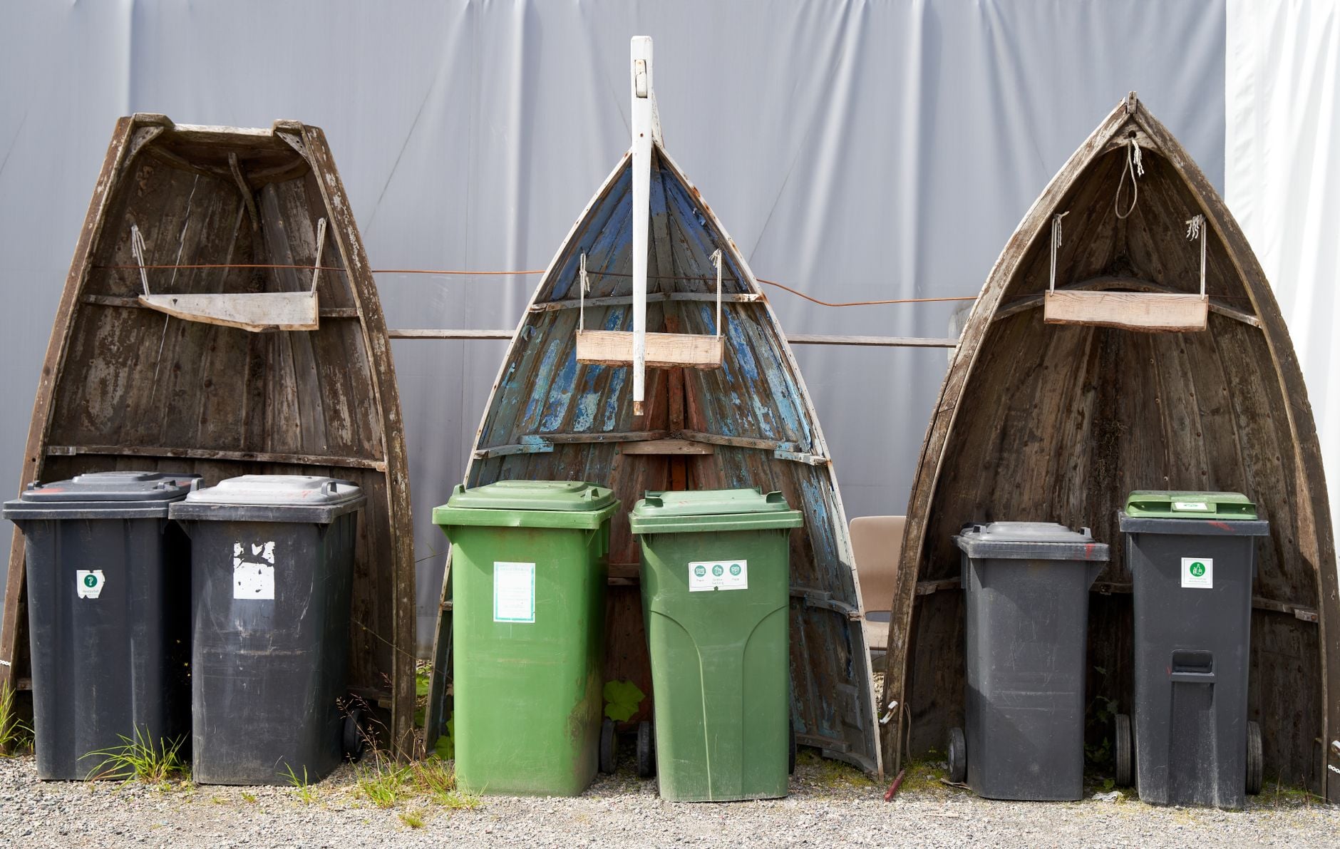 Recyclingbakken geplaatst in upcycled bootrompen creëren een artistieke buiteninstallatie.