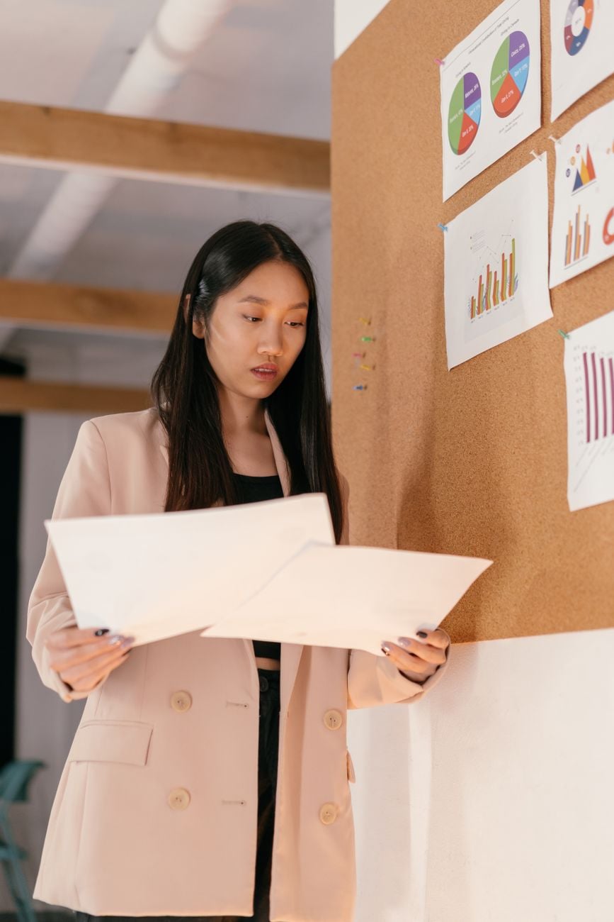 Aziatische vrouw in zakelijke outfit bekijkt businessanalytische grafieken op het prikbord.