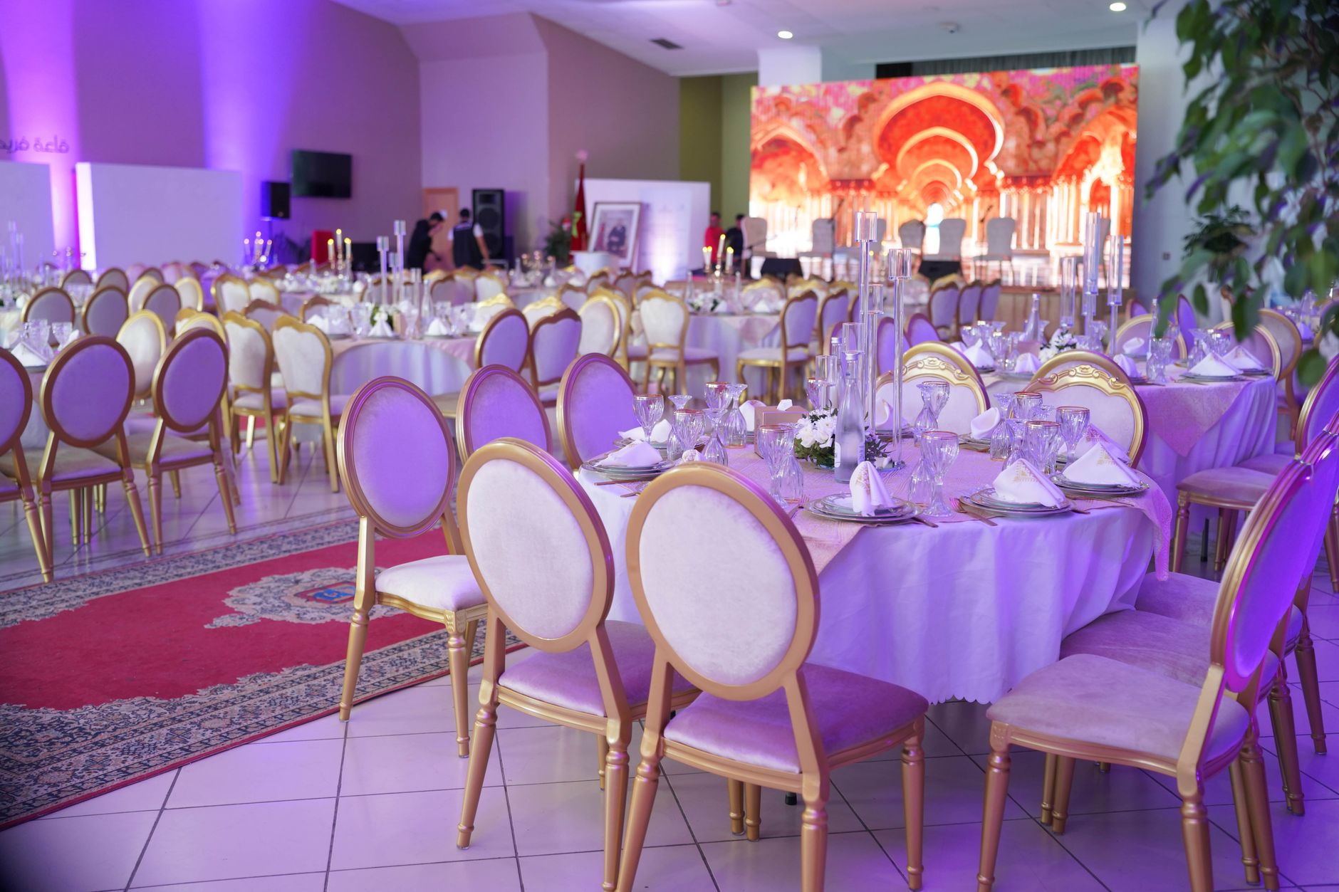 Luxe feestzaal ingericht voor een groot evenement met elegante decoraties, paarse verlichting en gerangschikte tafels.