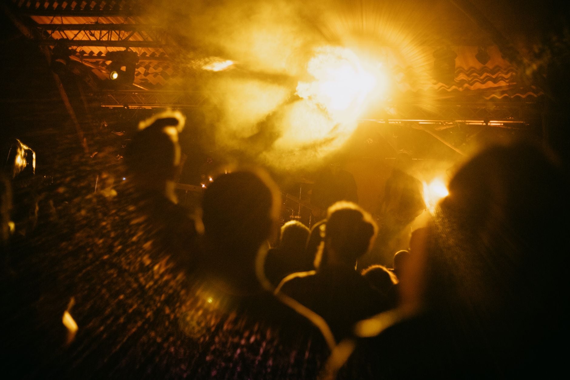 Een levendige menigte op een muziekconcert met heldere lichten en rookeffecten die een energieke sfeer creëren.