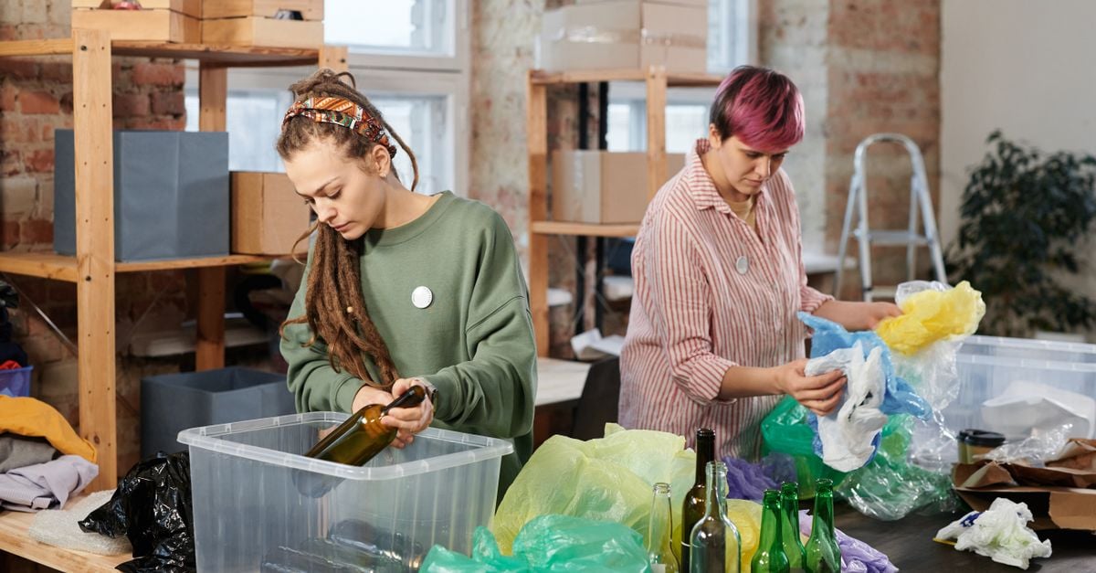 Two women sorting glass and plastic waste in an indoor recycling center.