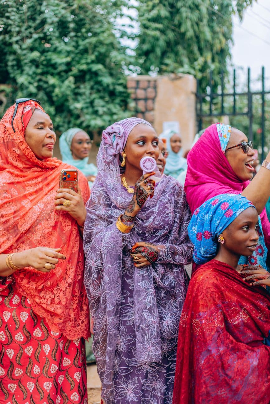 Een groep vrouwen in kleurrijke traditionele Afrikaanse kleding geniet van een bijeenkomst in de buitenlucht.