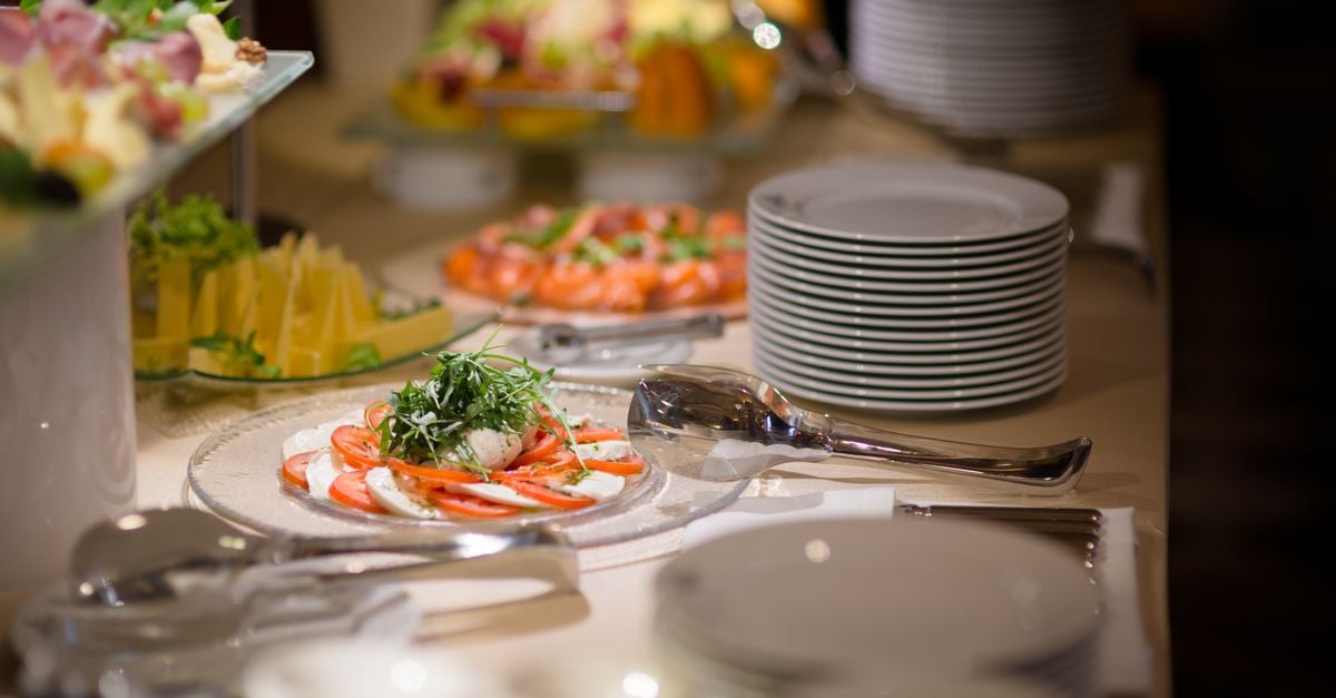 A beautifully arranged buffet with Caprese salad and fresh fruits on a white tablecloth.