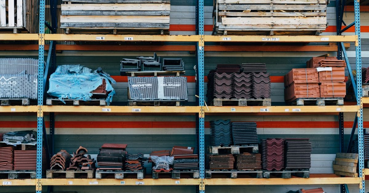 Shelves filled with construction materials like tiles and wood pallets in a warehouse setting.