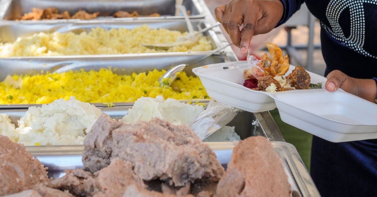 A person serves a variety of foods from a buffet station onto their plate.