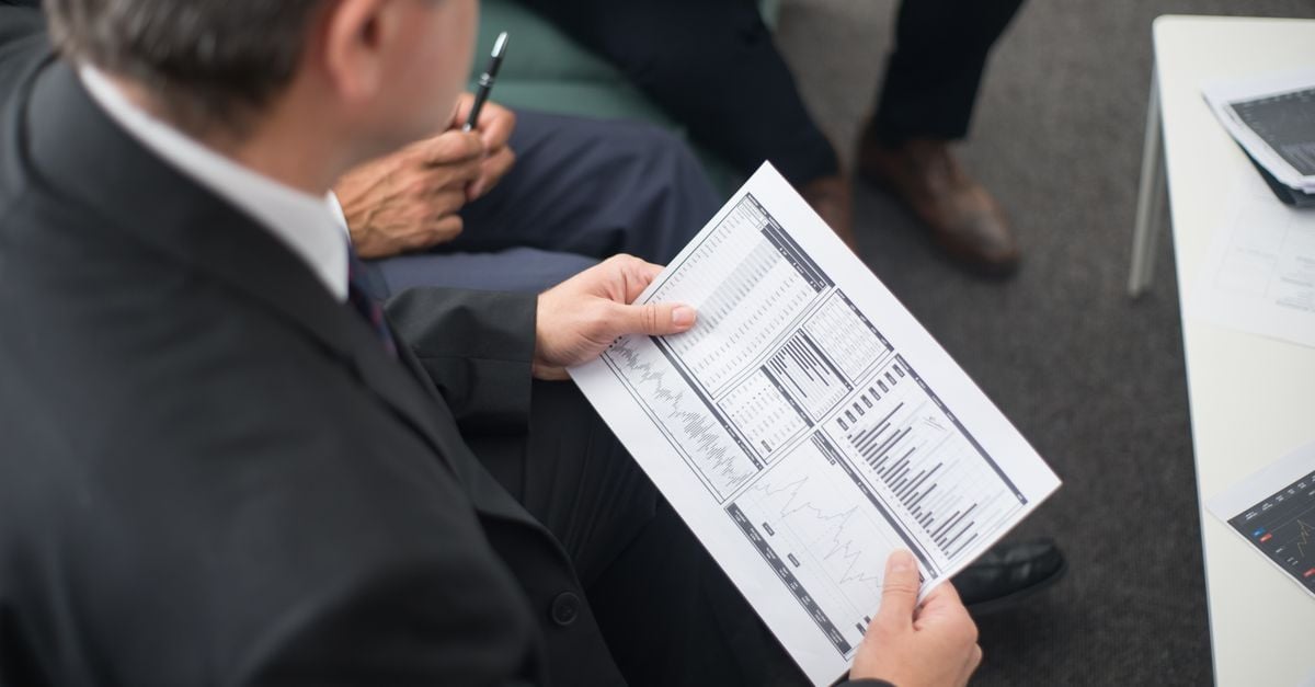 Two businessmen analyze financial documents during a meeting, focusing on data trends and performance.