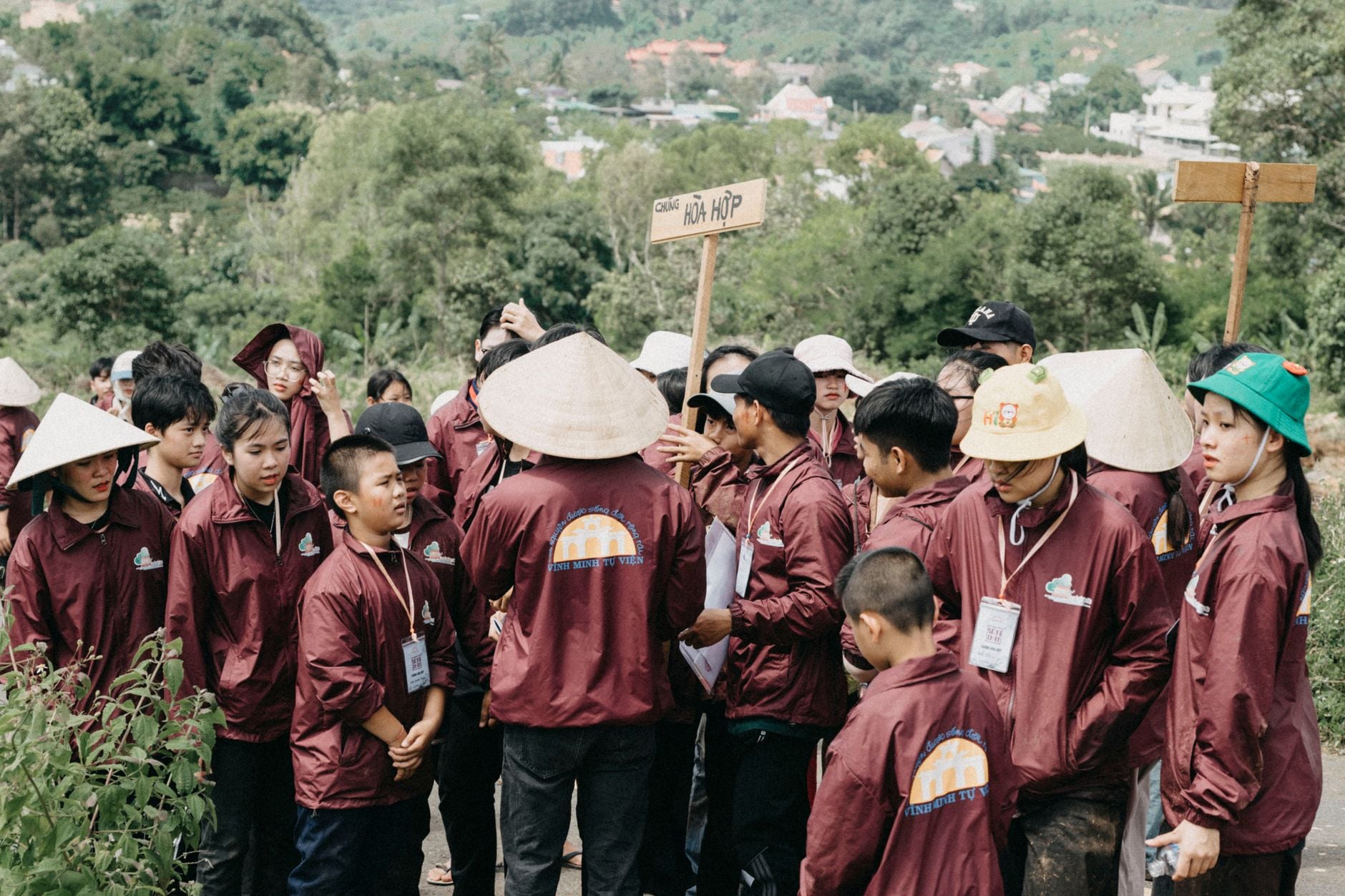 A diverse group of individuals in maroon uniforms gathered outdoors amidst lush greenery.