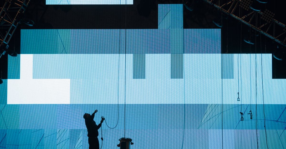 Side view of anonymous male worker silhouette setting up digital screen while looking up on stage